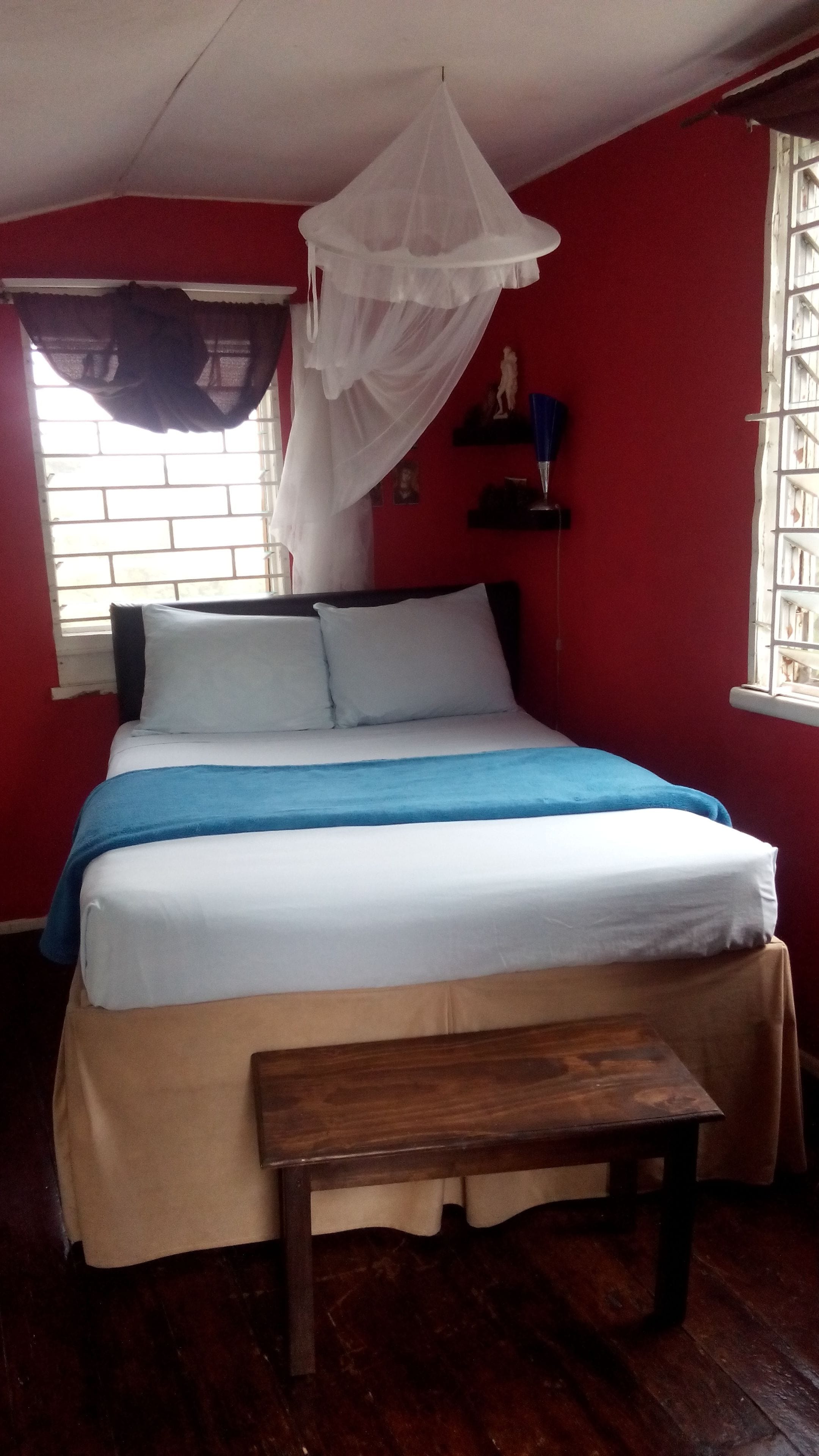 A bed with a white and blue bedspread, a wooden bench, a white canopy, and a red wall.