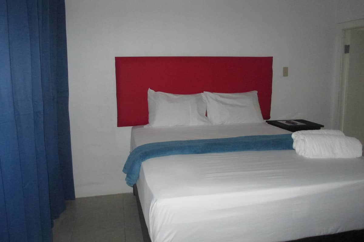 A hotel room with a bed, a red headboard, white bedding, and a blue curtain.