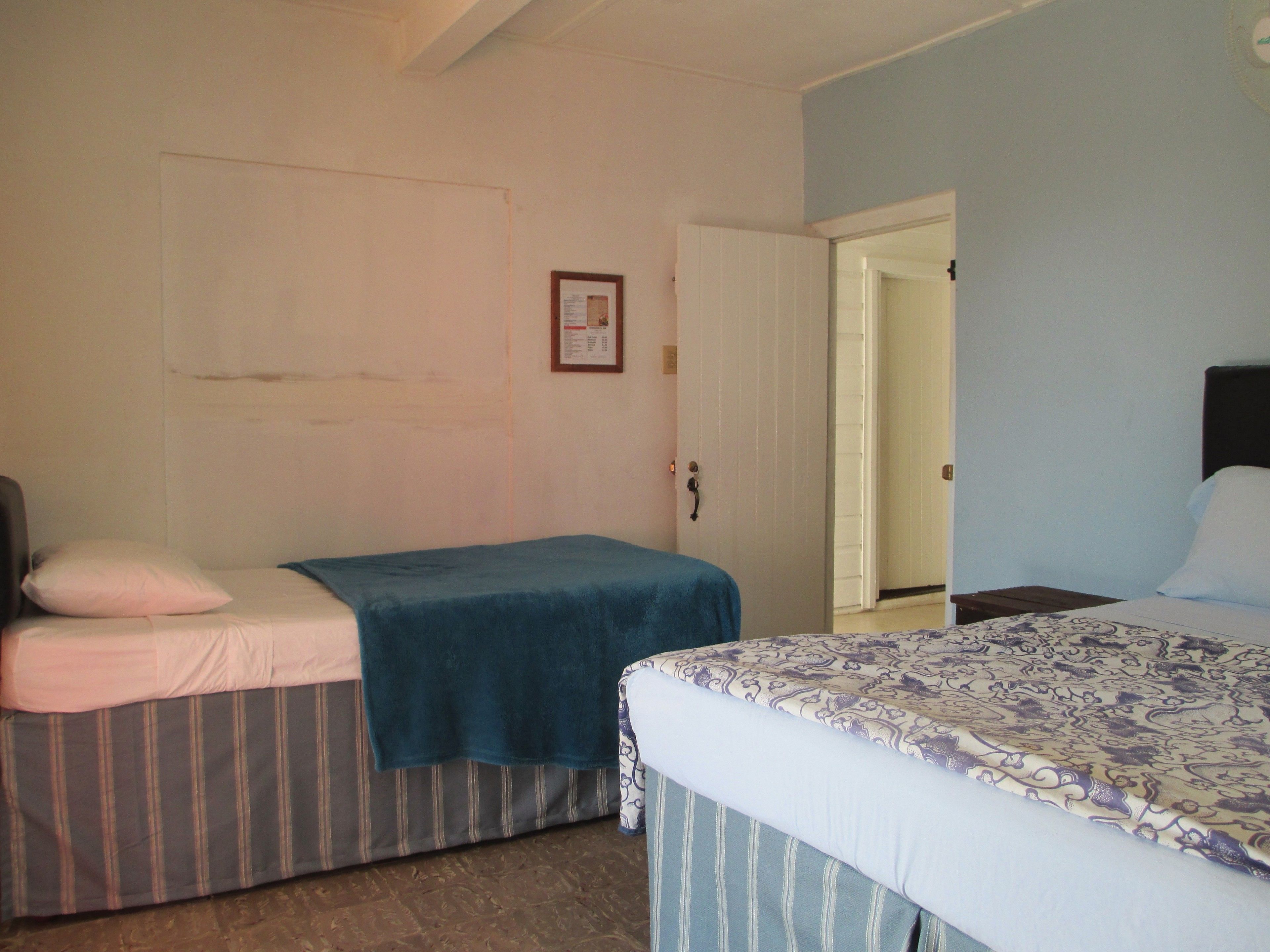 A room with two single beds, a wooden nightstand, a door, and a wall-mounted light switch.