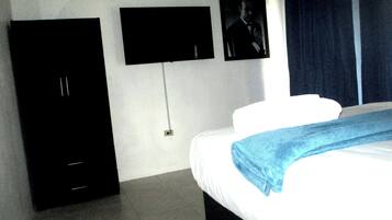 A hotel room with a bed, a flat-screen TV mounted on the wall, and a door.
