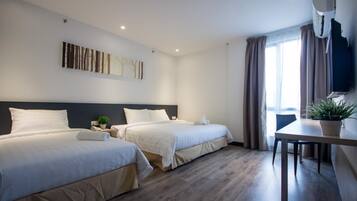 A hotel room with two beds, a desk, a potted plant, and a wall-mounted TV.