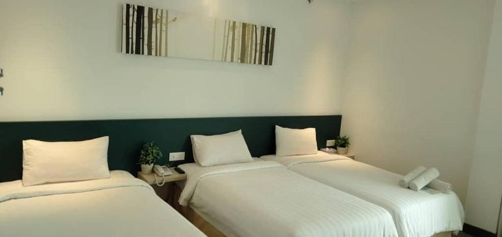 Une chambre d’hôtel avec deux lits, une tête de lit vert foncé, du linge de lit blanc et une œuvre d’art accrochée au mur.