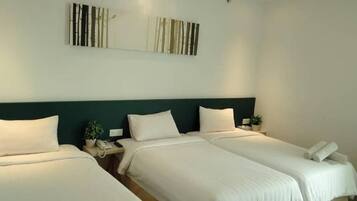 Une chambre d’hôtel avec deux lits, une tête de lit vert foncé, du linge de lit blanc et une œuvre d’art accrochée au mur.