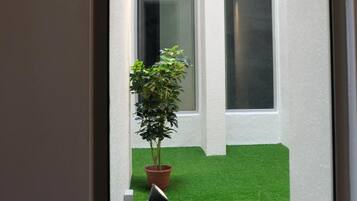 A view through a window of a building with a small artificial green lawn, a potted plant, and a black lamp.