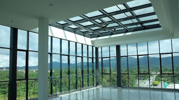 A spacious room with large windows and a skylight, offering a view of green hills and a road.