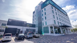 A multi-story hotel with a modern design, featuring a large glass facade and a parking area with several cars.