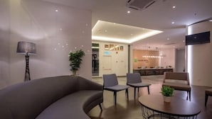 A modern hotel lobby with a curved sofa, two armchairs, a round table, and a potted plant.