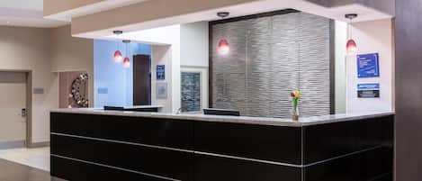 Un mostrador de recepción moderno con acabado negro, separador de vidrio e iluminación colgante.