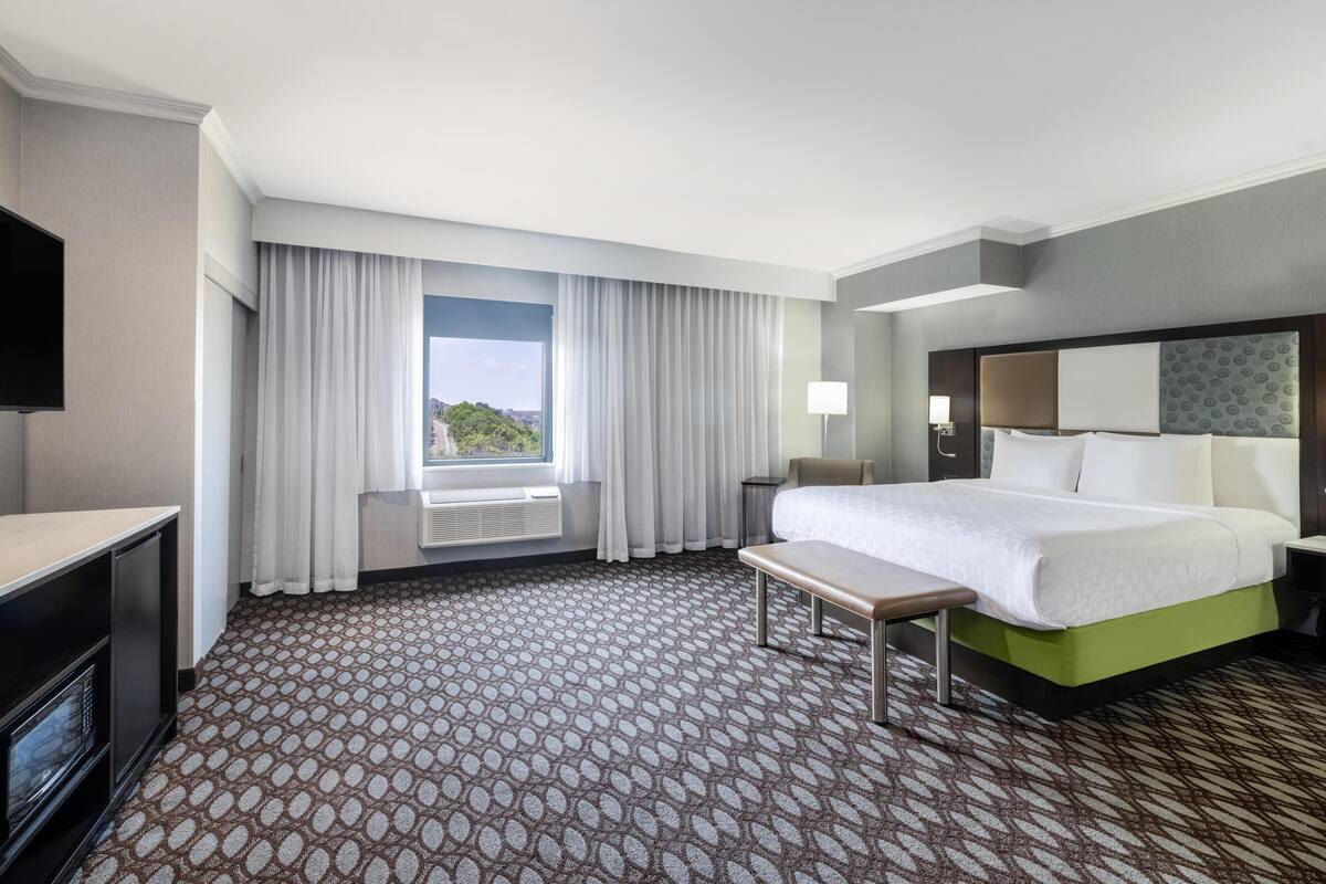 A hotel room with a large bed, a desk, a TV, and a window with curtains.