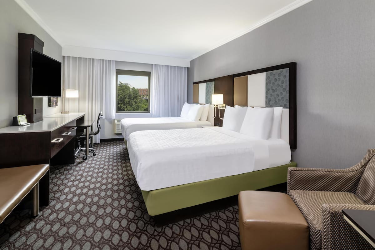 A hotel room with a large bed, a desk, a chair, a TV, and a window with curtains.