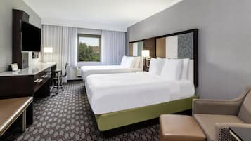 Habitación de hotel con una cama grande, un escritorio, una silla, un televisor y una ventana con cortinas.