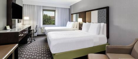 A hotel room with a large bed, a desk, a chair, a TV, and a window with curtains.