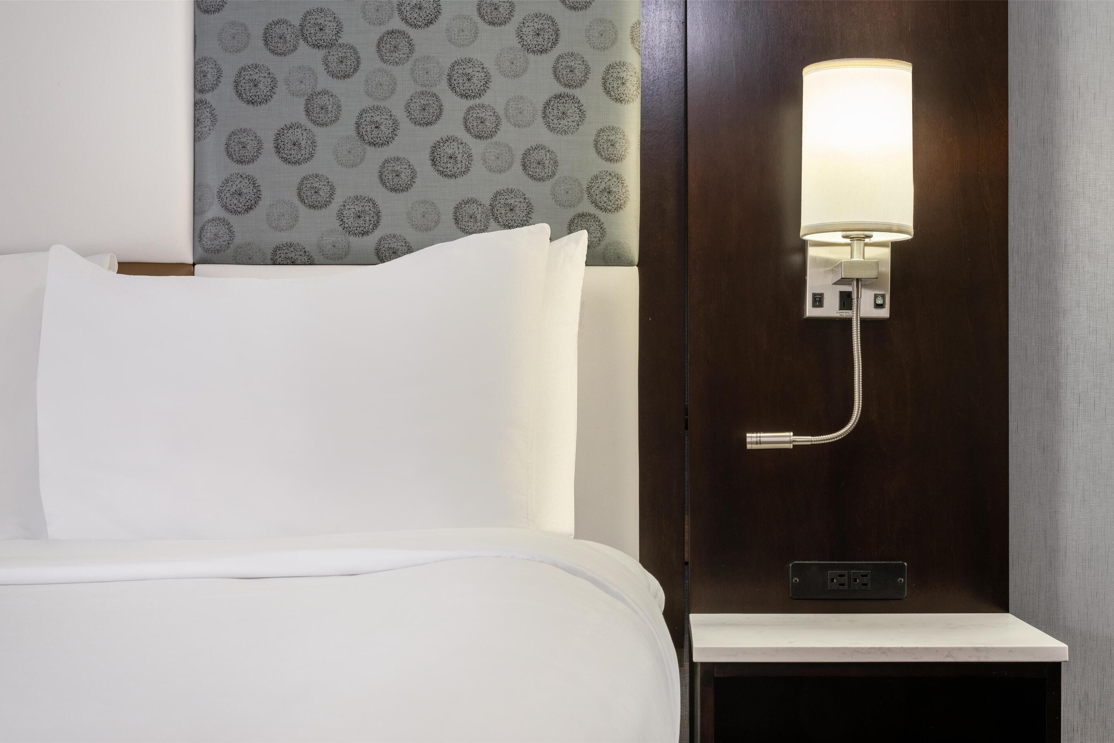 Una camera d'albergo con un letto rifatto, un comodino a parete con una lampada e carta da parati decorata.