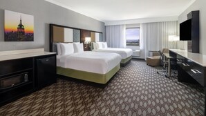 A hotel room with two beds, a desk, a TV, and a cityscape view.