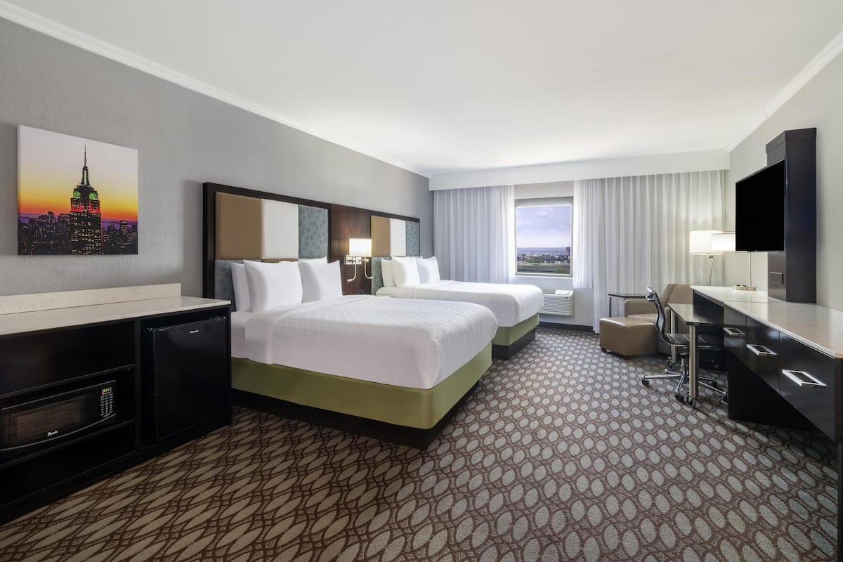 A hotel room with two beds, a desk, a TV, and a cityscape view.