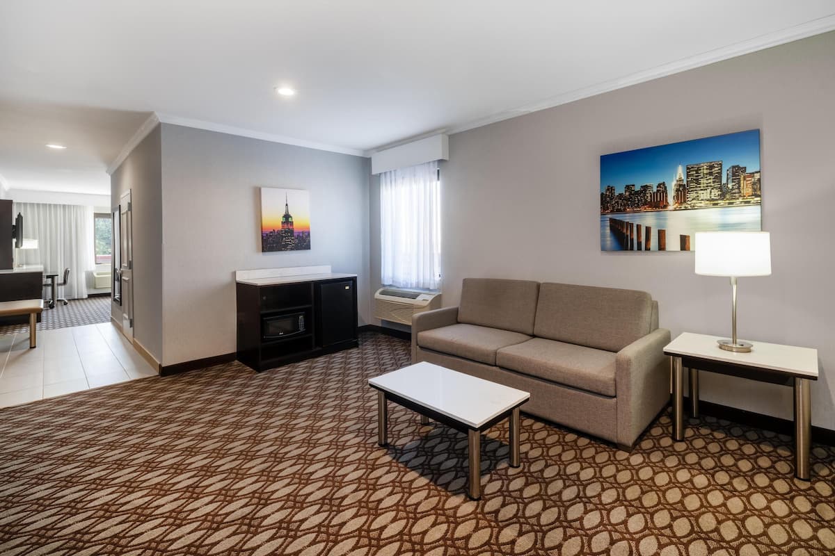 A hotel room with a patterned carpet, a sofa, a coffee table, a TV, and a painting of a cityscape.