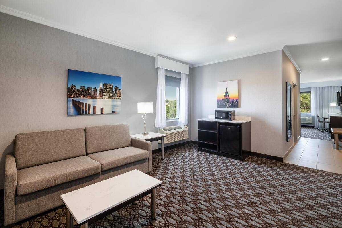 A hotel room with a sofa, a small table, a TV, and a cityscape painting on the wall.