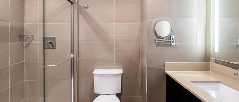 Un baño moderno con ducha de vidrio, inodoro blanco y tocador con espejo.