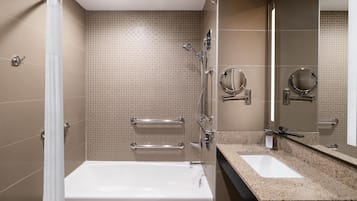 A modern bathroom with a bathtub, a shower with a glass door, a sink with a granite countertop, and two wall-mounted mirrors.