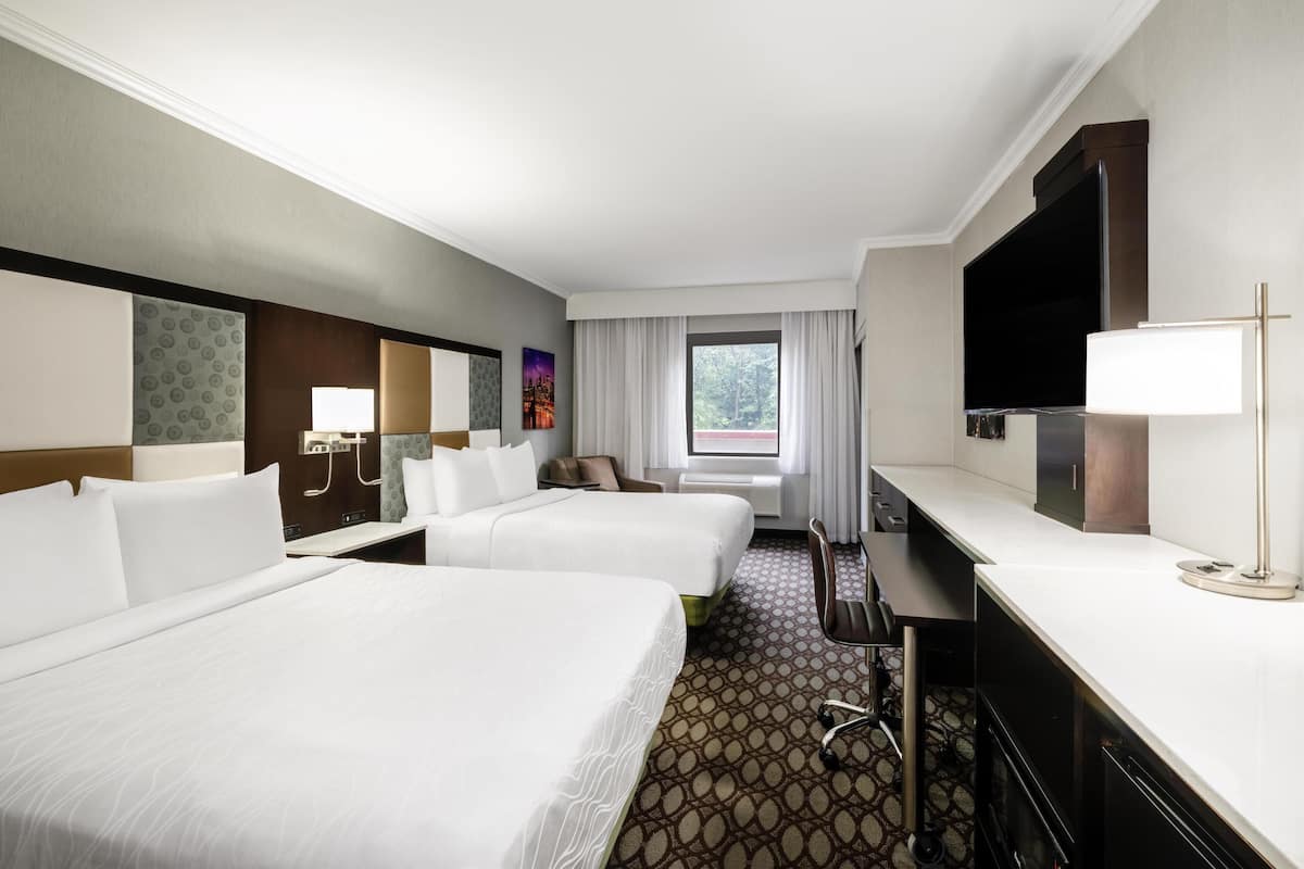 Une chambre d’hôtel avec deux lits, un bureau, une télévision et une fenêtre avec des rideaux.
