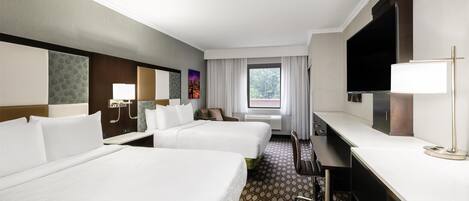 A hotel room with two beds, a desk, a TV, and a window with curtains.