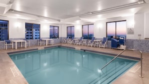 A pool area with clear blue water, lounge chairs, and tables.