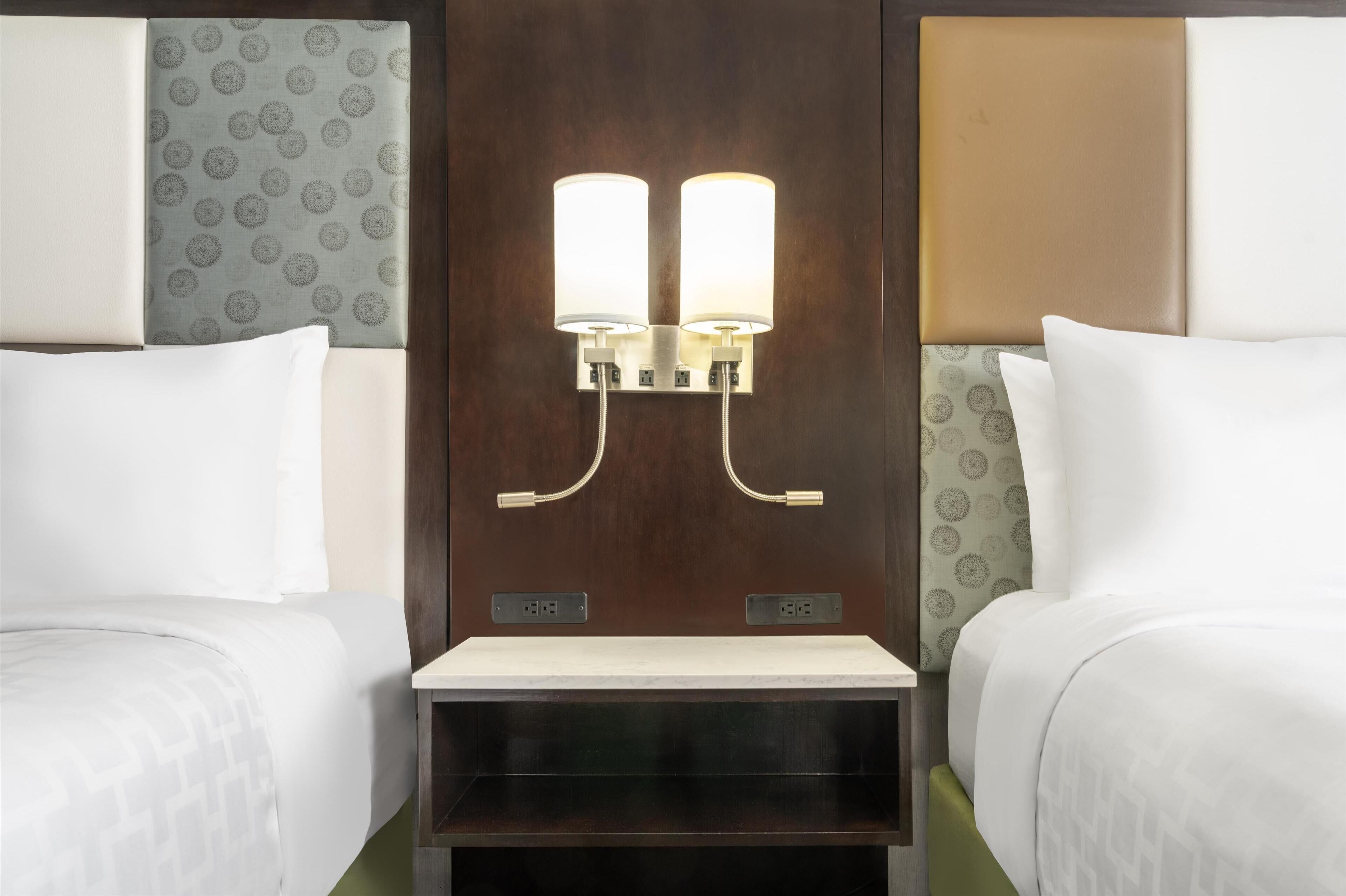 Une chambre d’hôtel avec deux lits, une table de chevet et un luminaire fixé au mur.