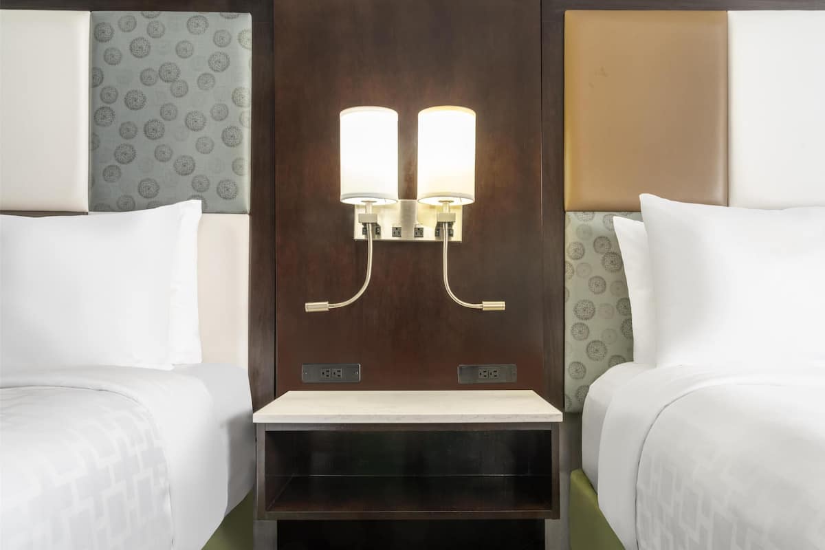 Une chambre d’hôtel avec deux lits, une table de chevet et un luminaire fixé au mur.