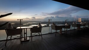 A balcony with wicker chairs and a table, overlooking a body of water and a bridge. - Wyndham Panbil Batam (Batam)
