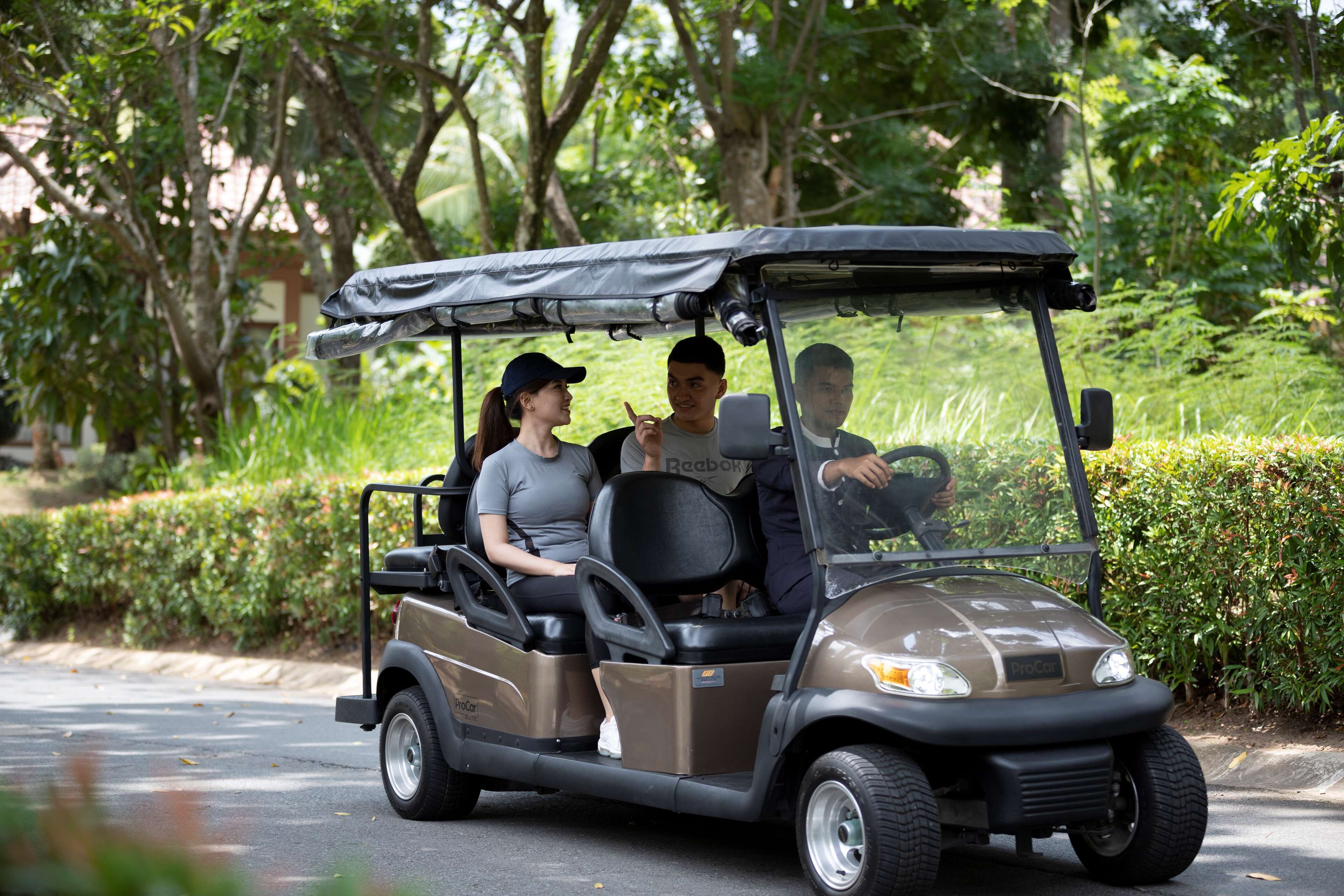 A golf cart with three passengers on a paved road surrounded by greenery.