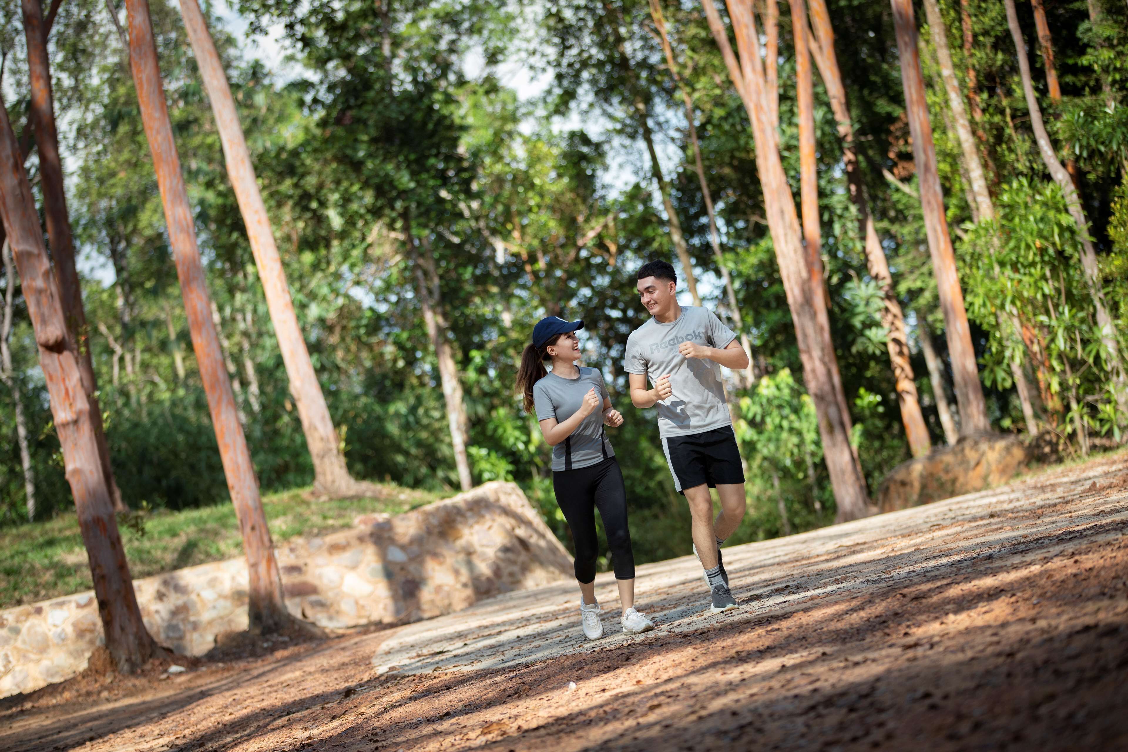 Two people jogging on a dirt path surrounded by trees.
