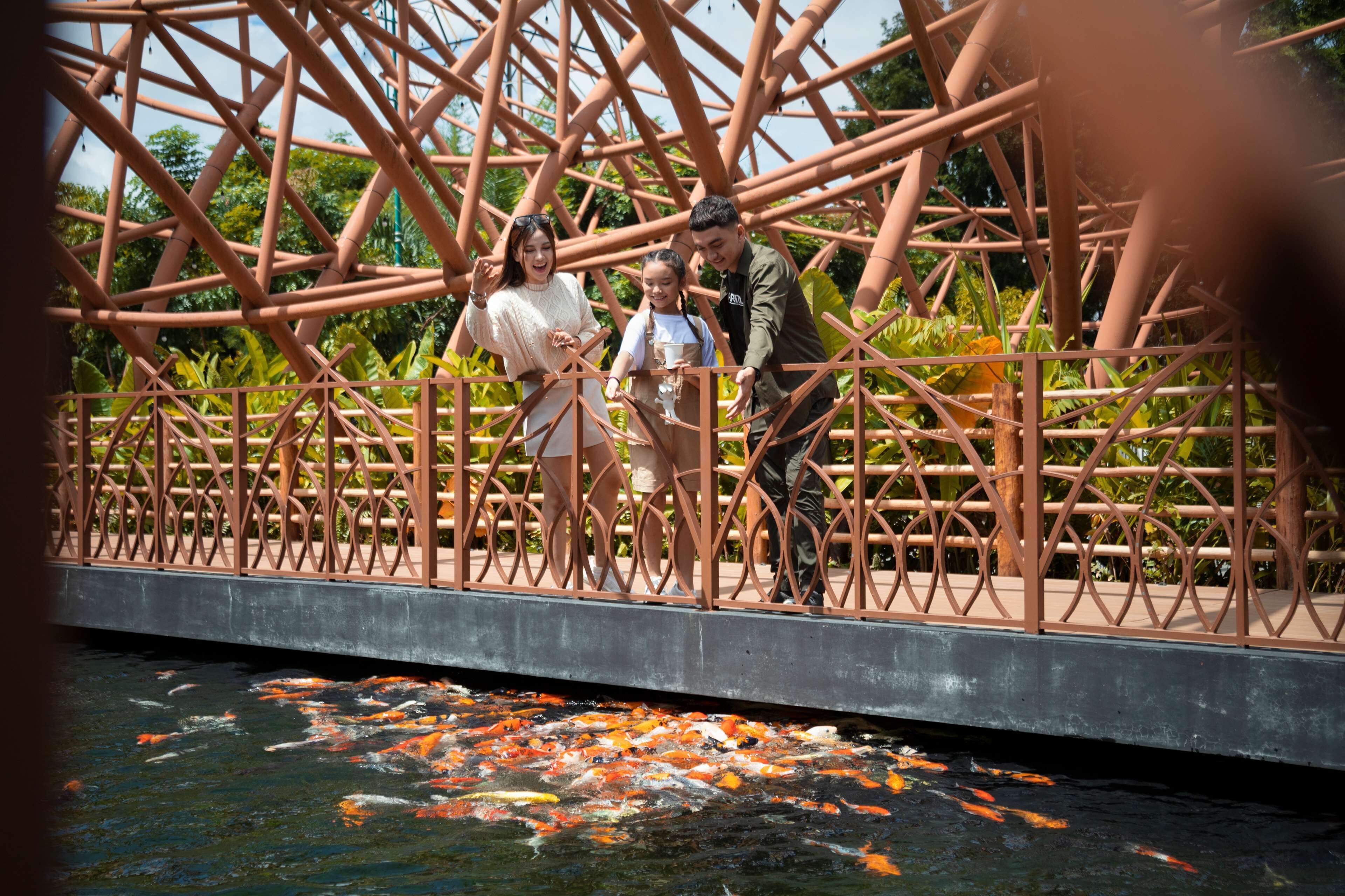 A bridge with a metal railing and koi fish swimming below.