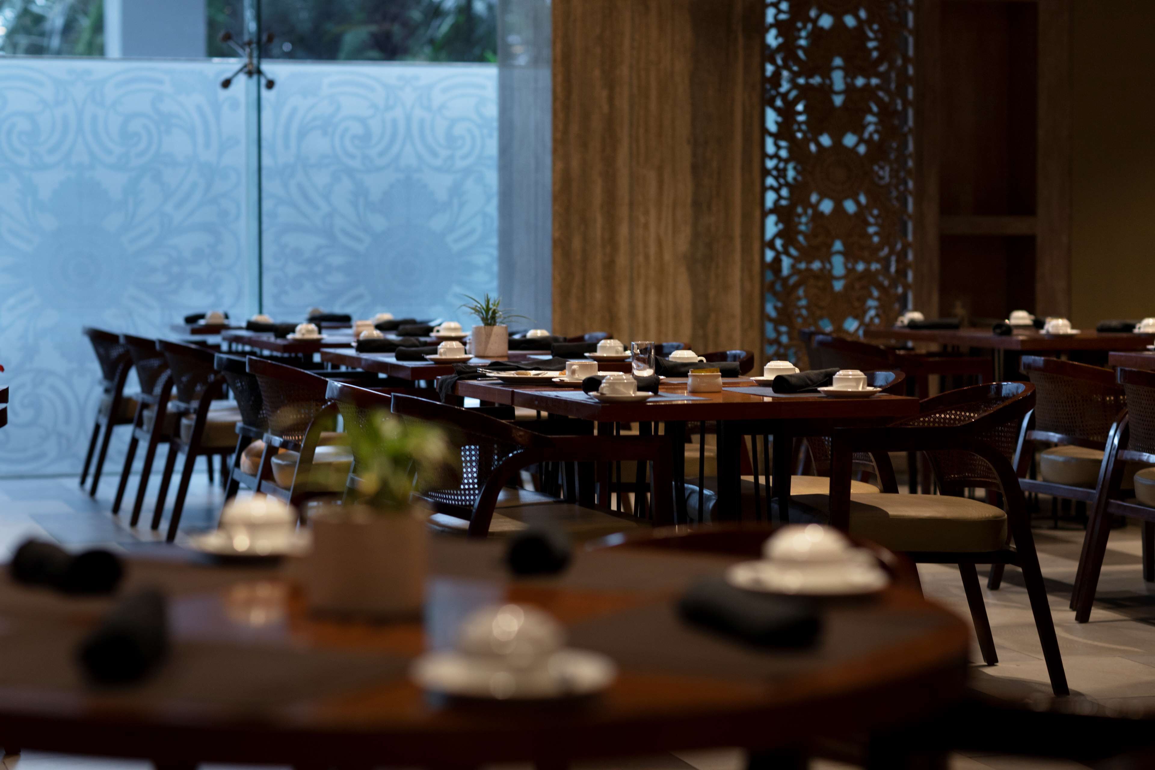 A restaurant with multiple tables set for dining, featuring a modern interior design with wooden furniture and decorative elements.
