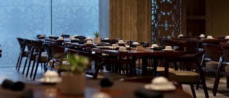 A restaurant with multiple tables set for dining, featuring a modern interior design with wooden furniture and decorative elements.