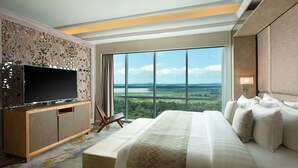 A hotel room with a large bed, a television on a wooden cabinet, and a view of a landscape through large windows. - Wyndham Panbil Batam (Batam)