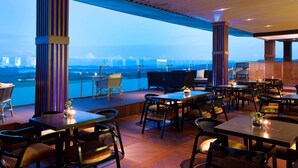 A rooftop restaurant with tables and chairs, a view of the city skyline, and a wooden ceiling structure. - Wyndham Panbil Batam (Batam)