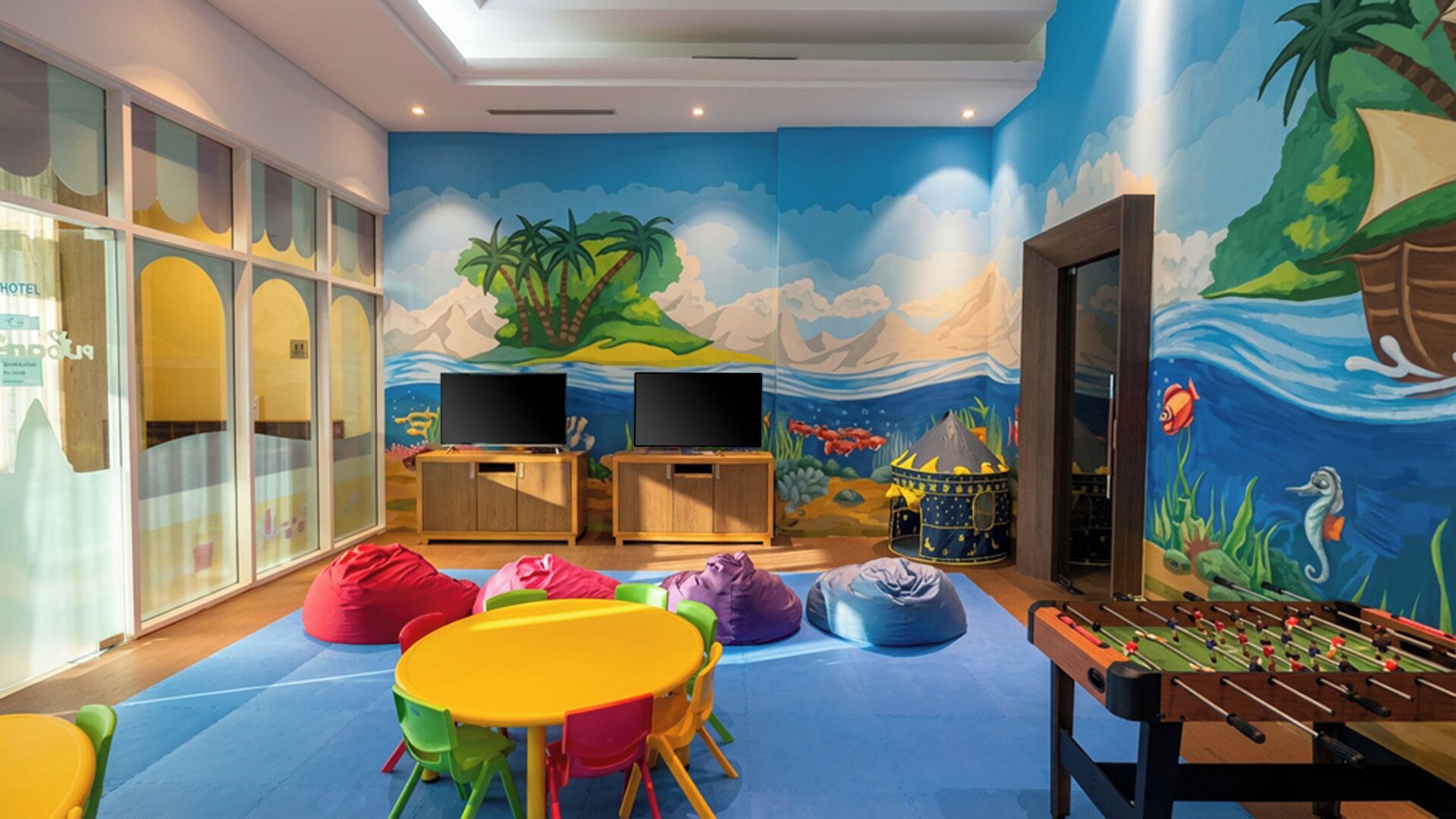 A children's play area with colorful furniture, a foosball table, and a mural depicting a tropical scene.