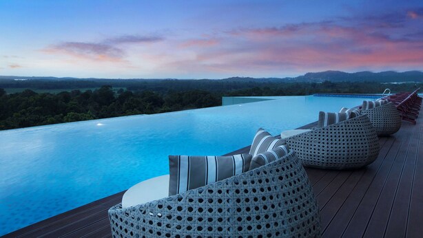 A poolside area with lounge chairs and a view of a natural landscape. - Wyndham Panbil Batam (Batam)