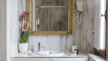 A bathroom with a marble vanity, a gold-framed mirror, a potted orchid, and a towel rack.