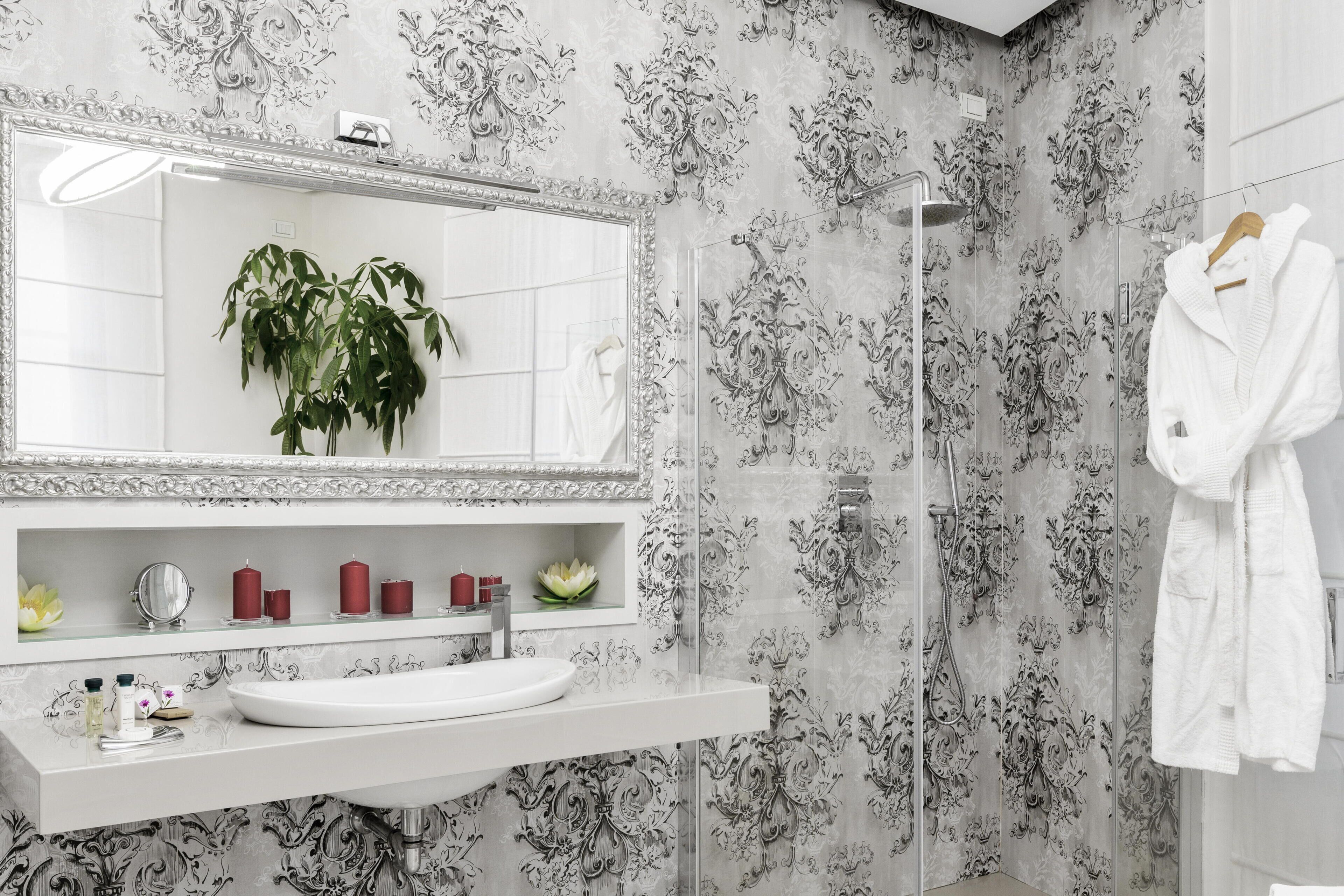 Ein Badezimmer mit einem weißen Waschbecken, Spiegel und Dusche. Auf der Ablage steht eine Pflanze und ein Handtuch hängt an der Wand.