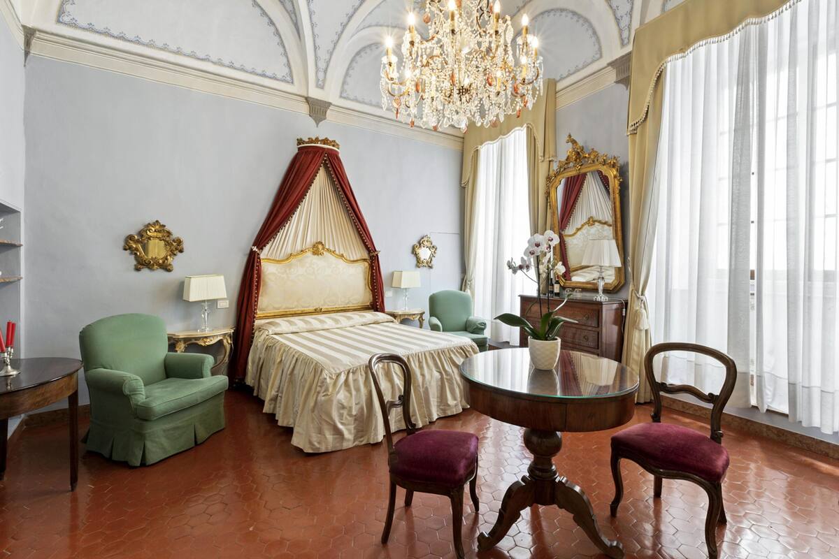 A luxurious bedroom with a large bed, a chandelier, and a mirror.