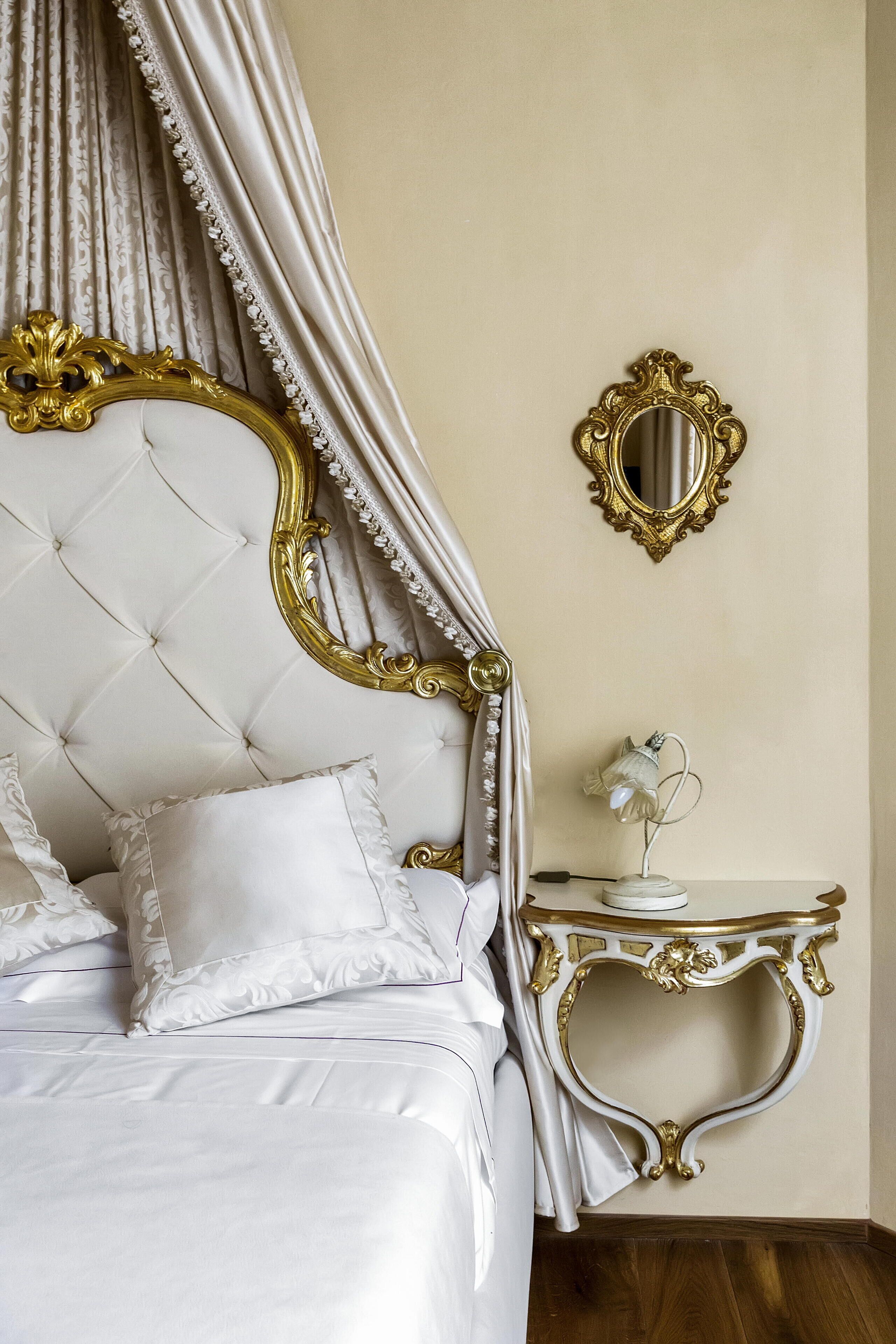 A luxurious bedroom with a tufted headboard, ornate gold frame, and a small bedside table with a lamp.