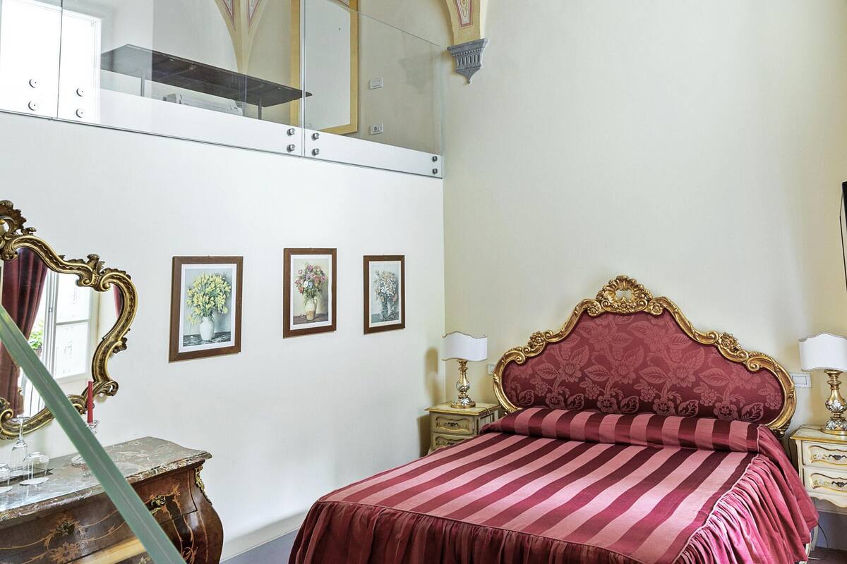 A bedroom with a checkered floor, a bed with a striped bedspread, a mirror, and framed pictures on the wall.
