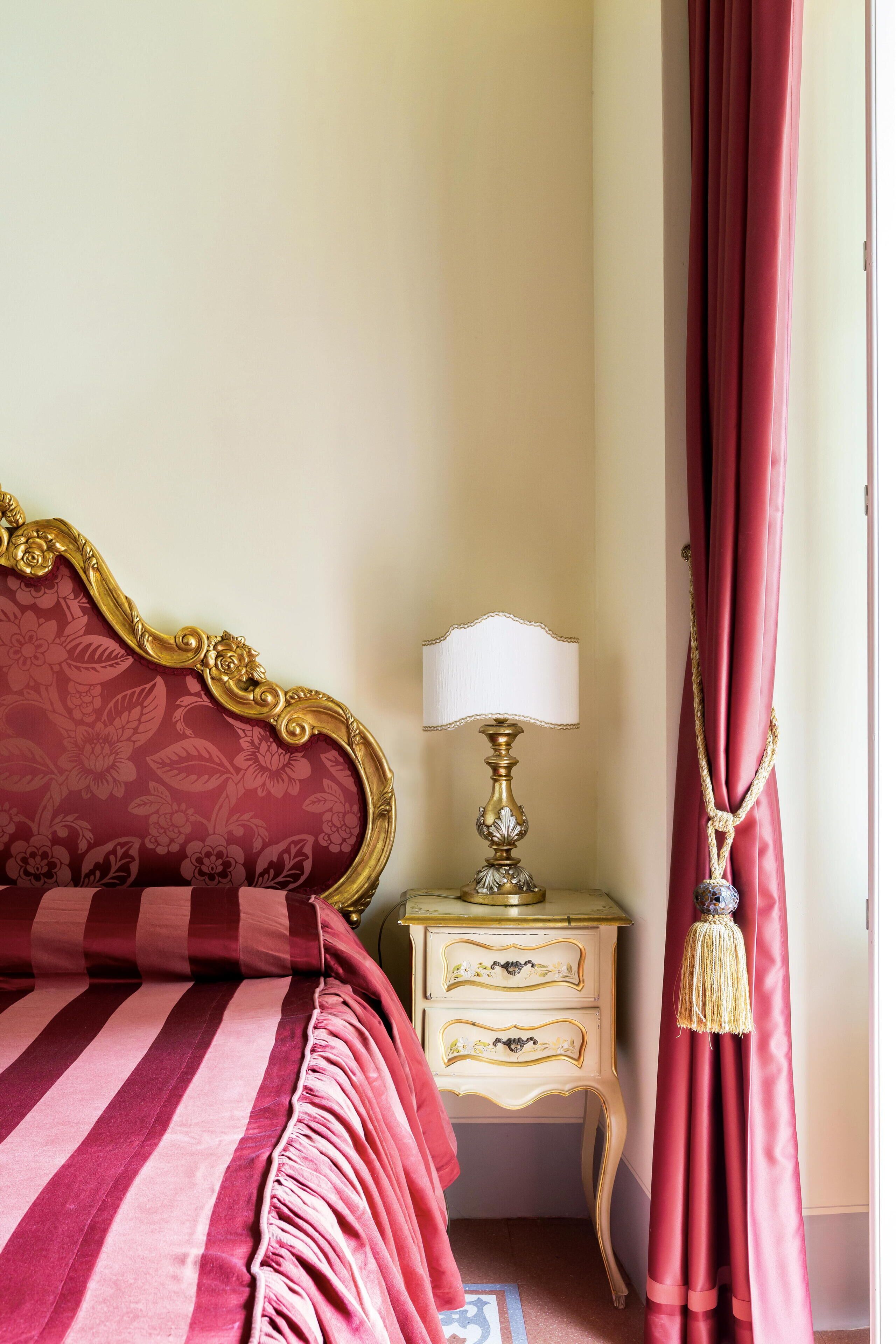 A bed with a red and gold headboard, a bedside table with a lamp, and a red curtain.