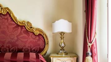 A bed with a red and gold headboard, a bedside table with a lamp, and a red curtain.