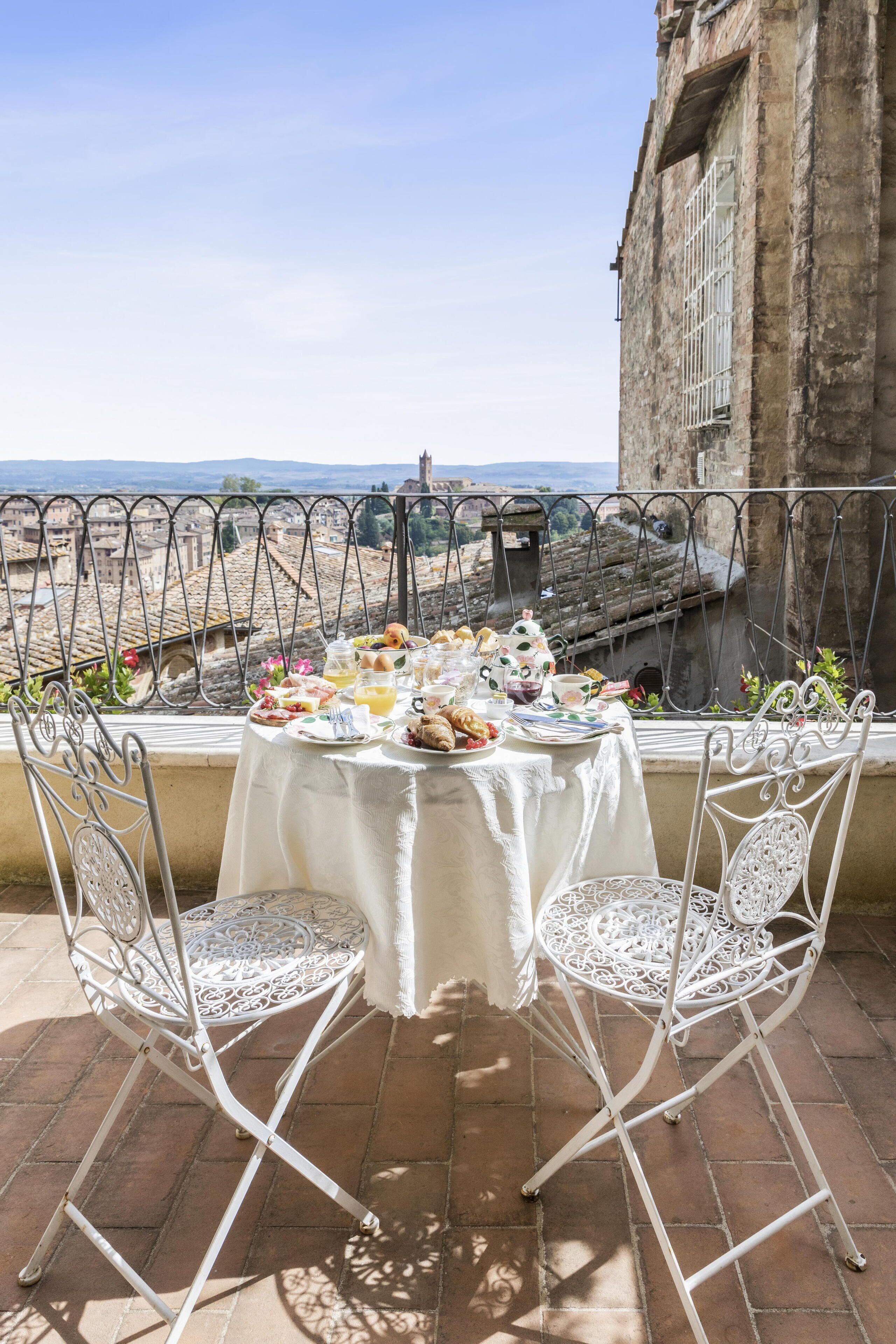 Une table dressée avec des aliments pour le petit-déjeuner, placée sur un balcon donnant sur une ville historique.