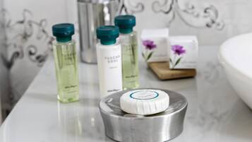 A bathroom vanity with a marble countertop, a metallic soap dish, and toiletries including a bottle of Tuscaran Soul body wash, a green bottle, and a bar of soap.