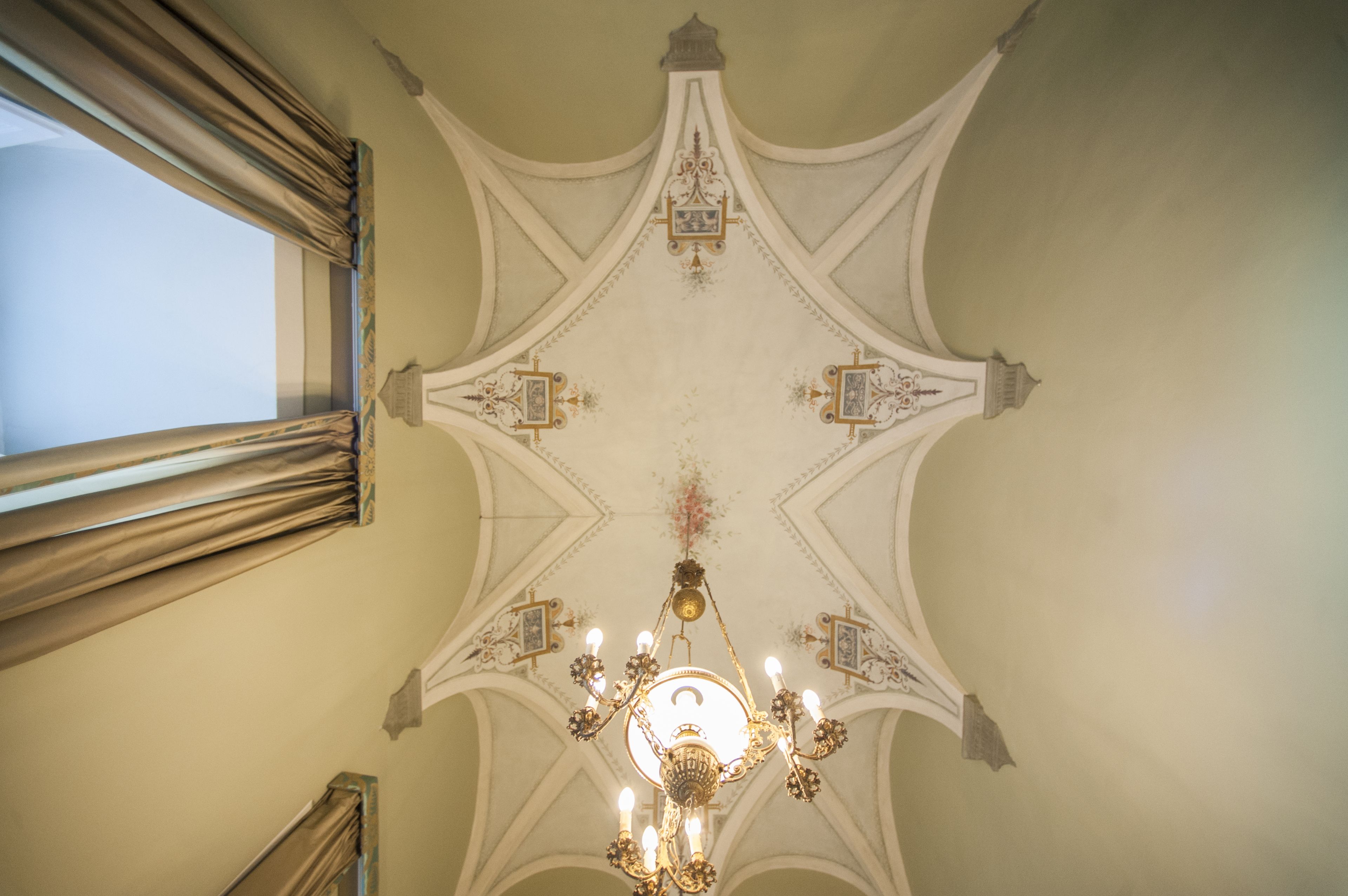 A chandelier with multiple light fixtures and ornate decorations on a ceiling with a star-like pattern.