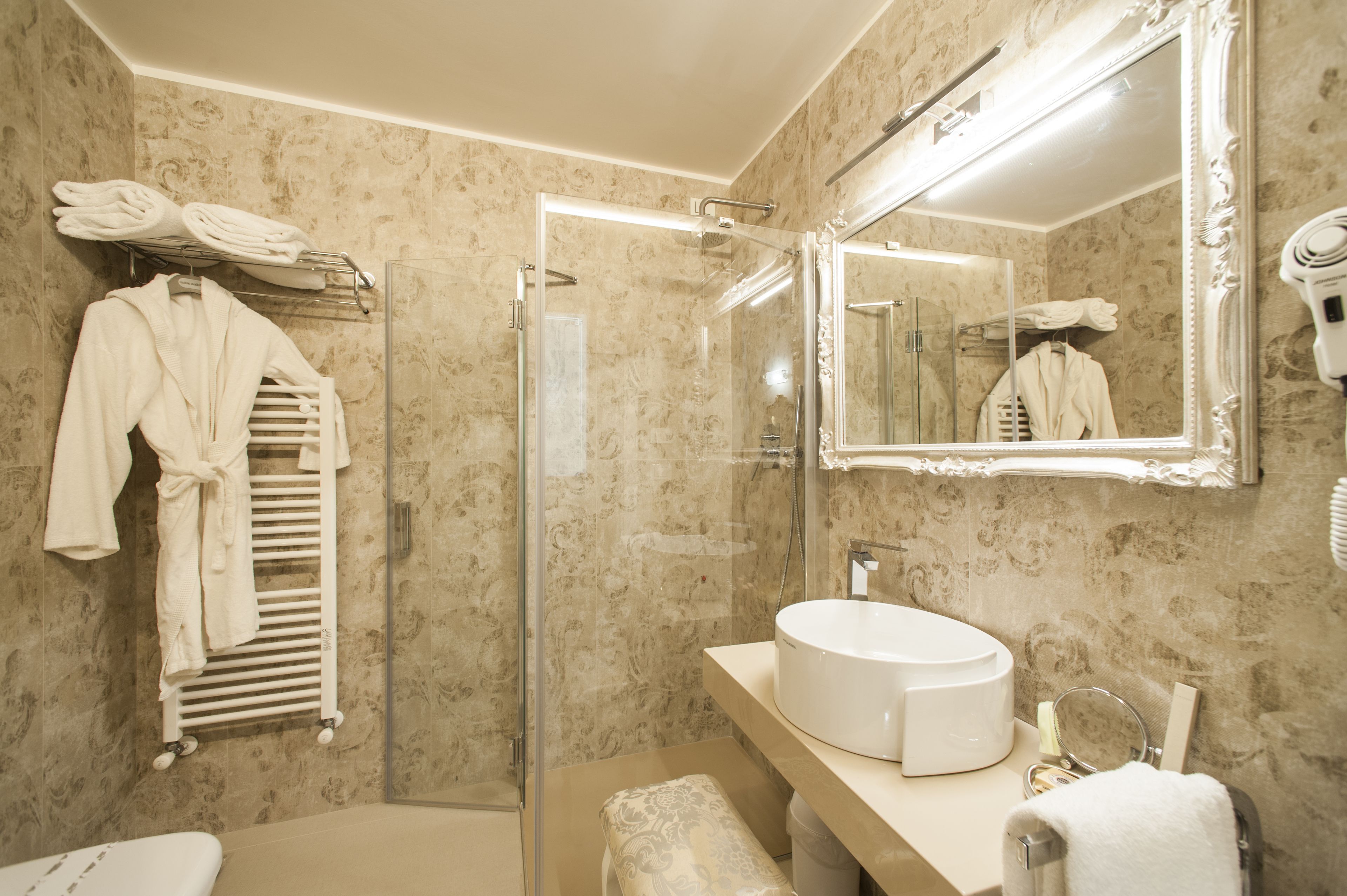 Casa de banho com cabine de chuveiro em vidro, lavatório branco e espelho com moldura decorativa.