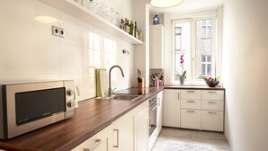 Una cocina moderna con microondas integrado, electrodomésticos de acero inoxidable, encimera de madera y ventana con vista a un edificio.